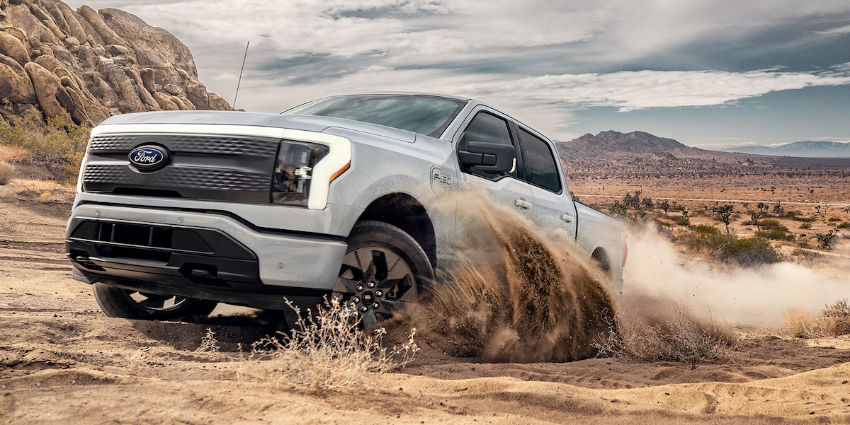 2025 Ford F-150 Lightning kicking up sand while off-roading in a desert landscape, showcasing its electric power and rugged capability near University Ford in Huntington, WV.