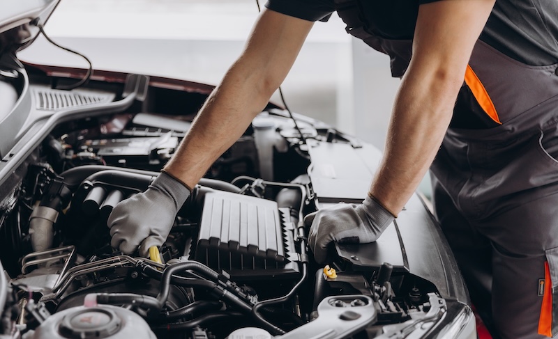 Close-up shot of unrecognisable man wearing gray glove inspecting car engine and interior of hood of car